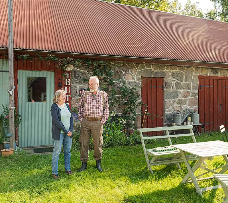 Ulla och Thomas står framför sin butik en solig sommardag. Huset är gjort av sten, med röda trädörrar